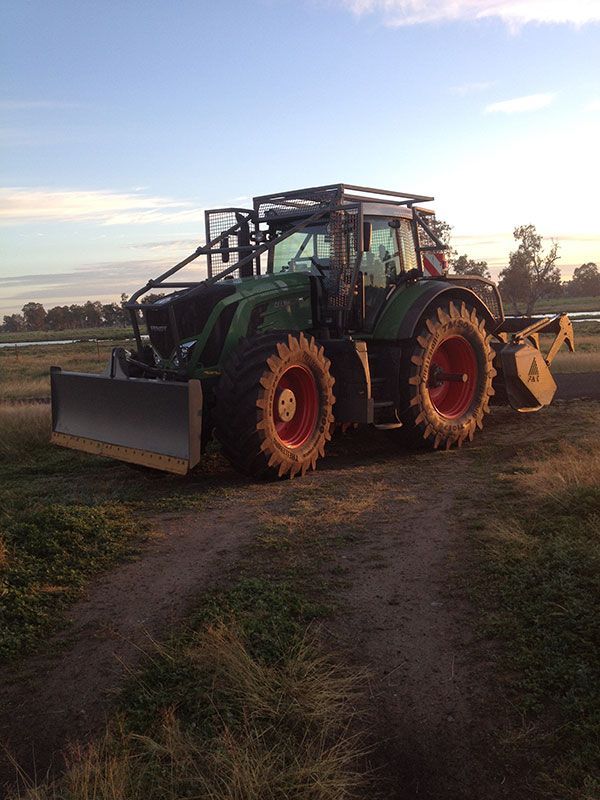 A green tractor with a bulldozer attached to it is parked in a field.