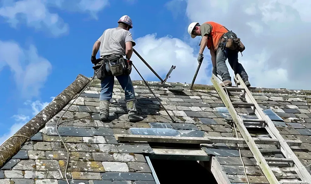 Two men are working on an old slate roof of a building.