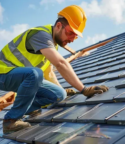 A man wearing a hard hat and safety vest is working on a tiled roof.