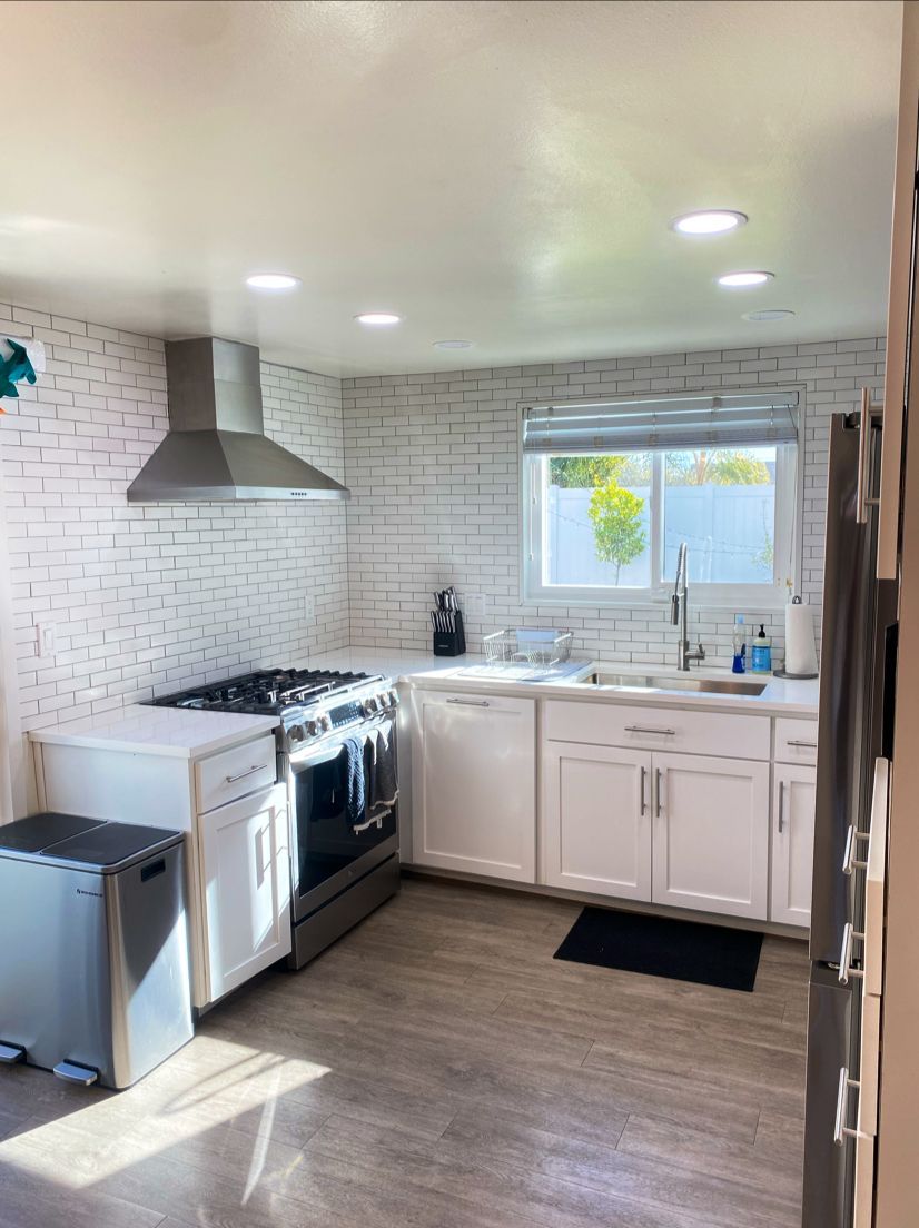 A kitchen with white cabinets , a stove , a sink , and a window.