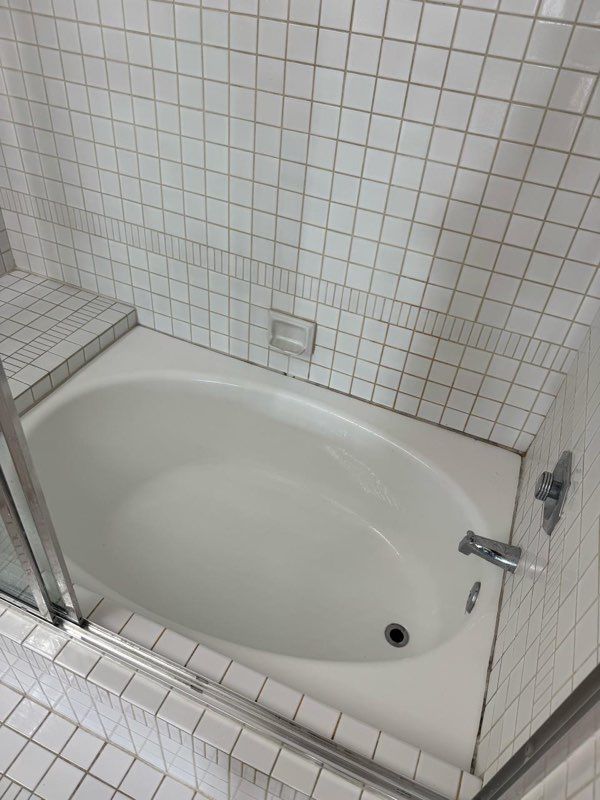 A bathtub in a bathroom with white tiles and a glass door.