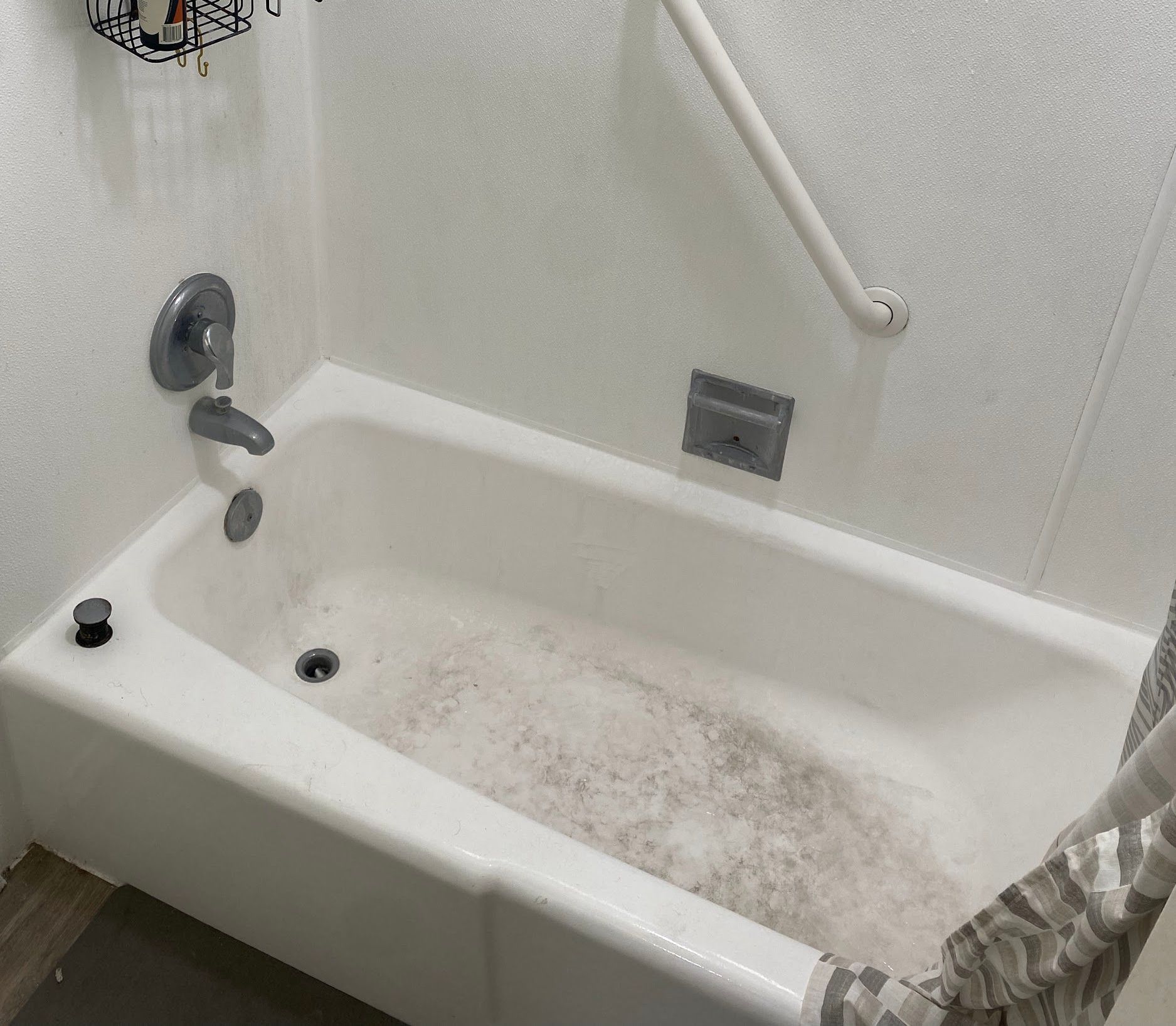 A bathtub in a bathroom with a shower curtain and a hand rail.