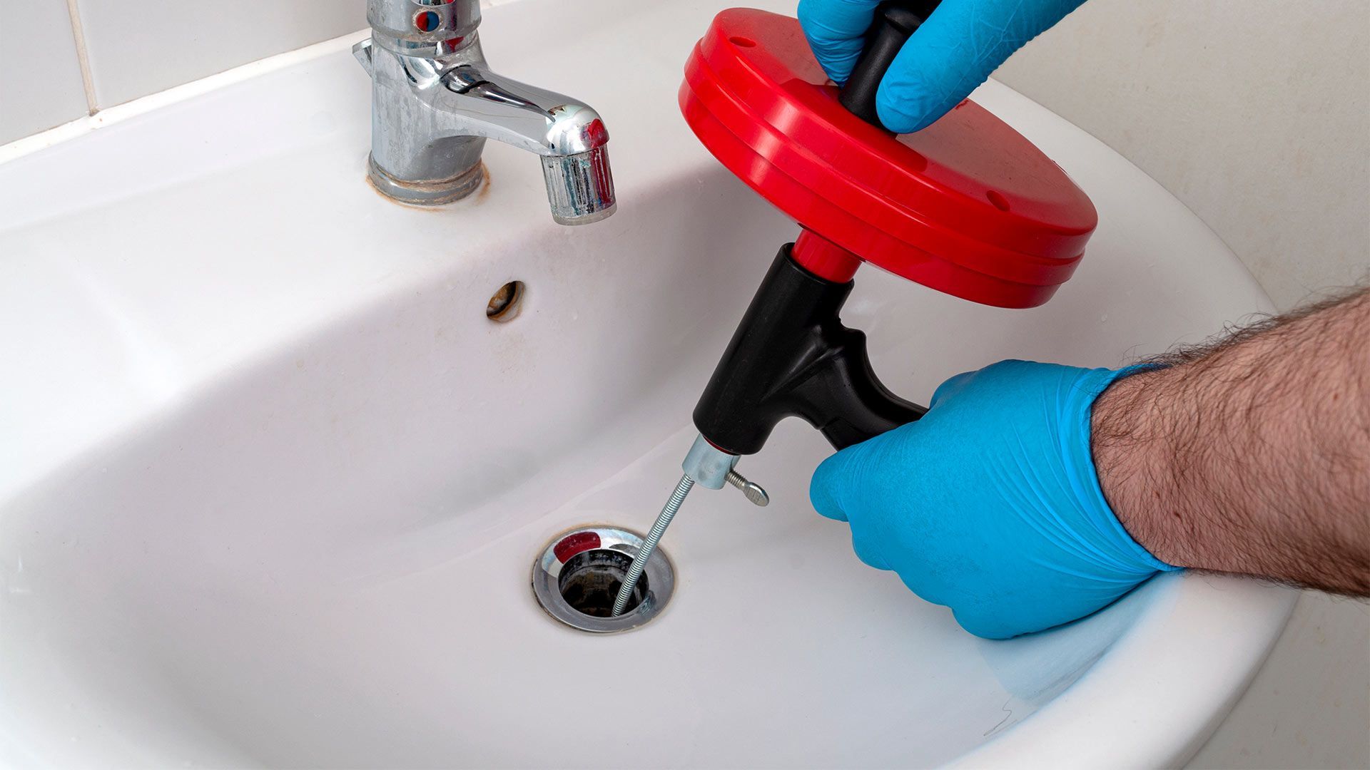 A person is using a drain snake to unblock a sink.