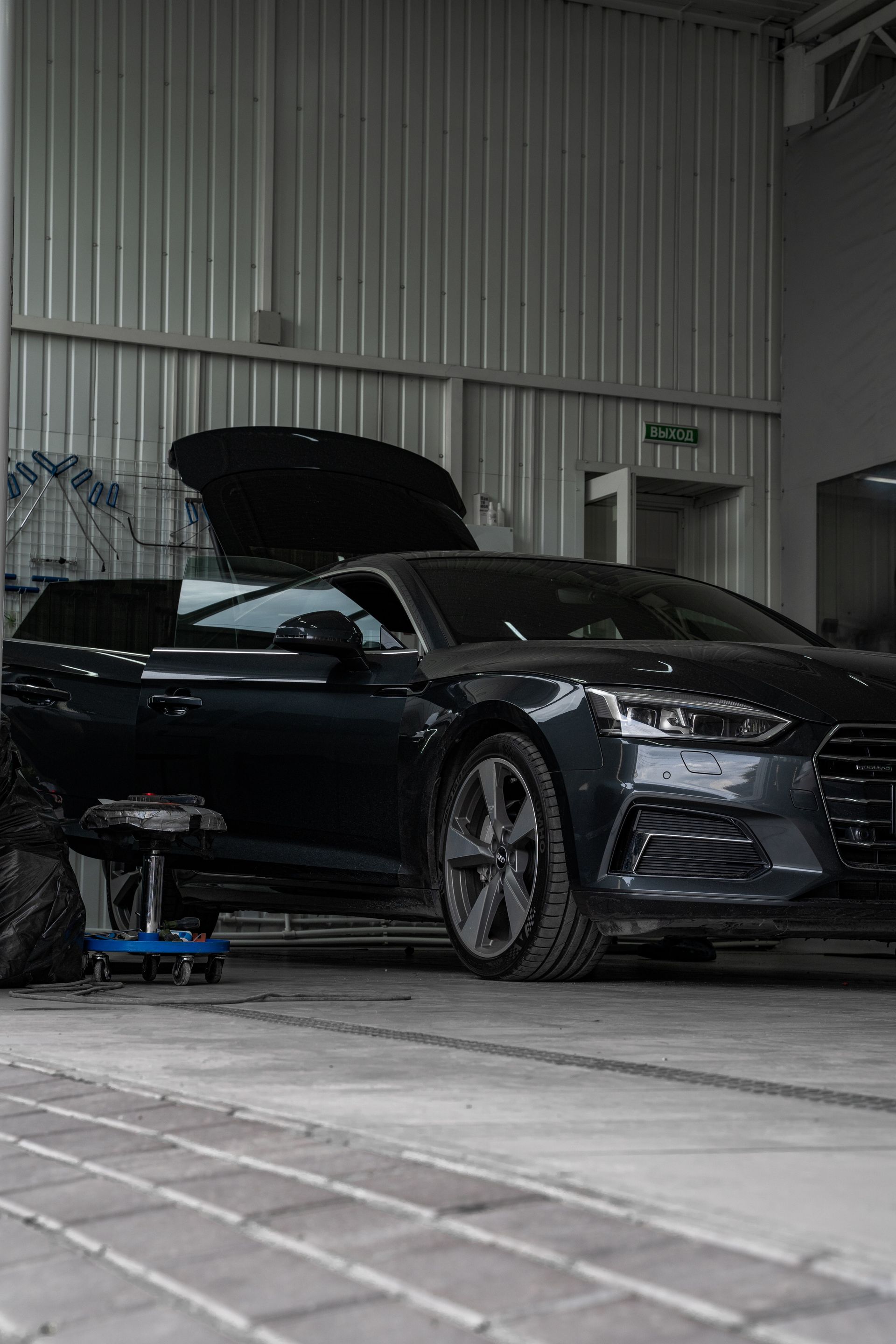 A black car with the hood up is parked in a garage.