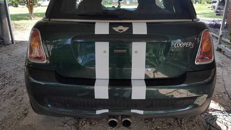 A green mini cooper with white stripes on the back is parked in a garage.