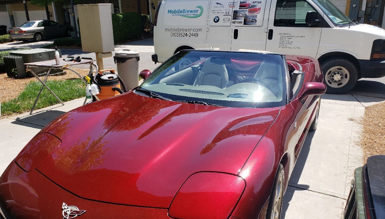 A red sports car is parked in a driveway next to a white van.