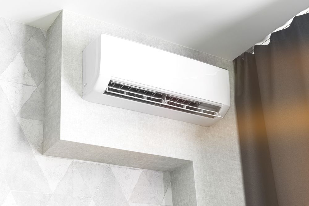 White air conditioner mounted on a light gray wall, near a brown curtain.
