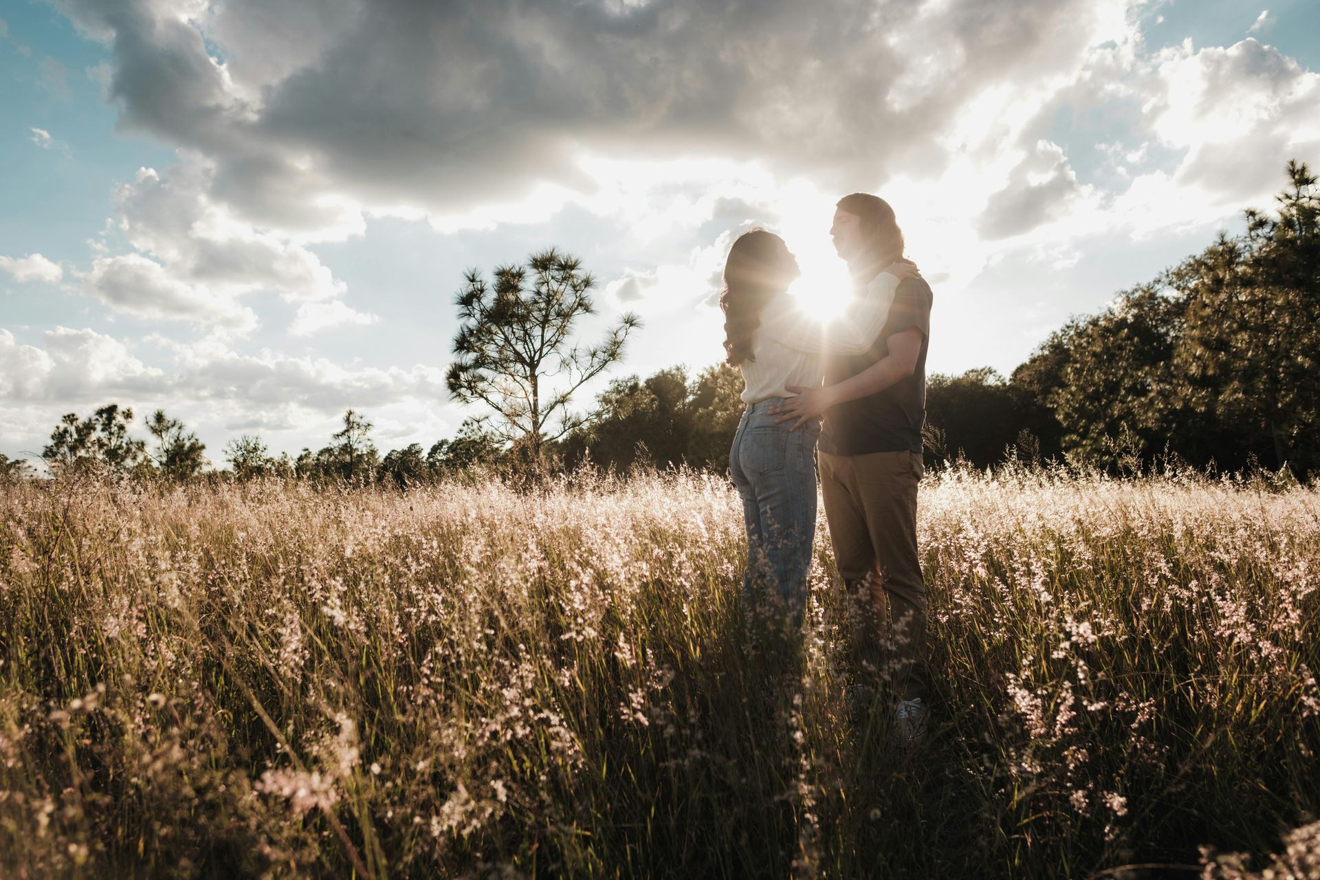 Couple holding hands in a sunlit field; backlit by the sun, obscured figures in silhouette.