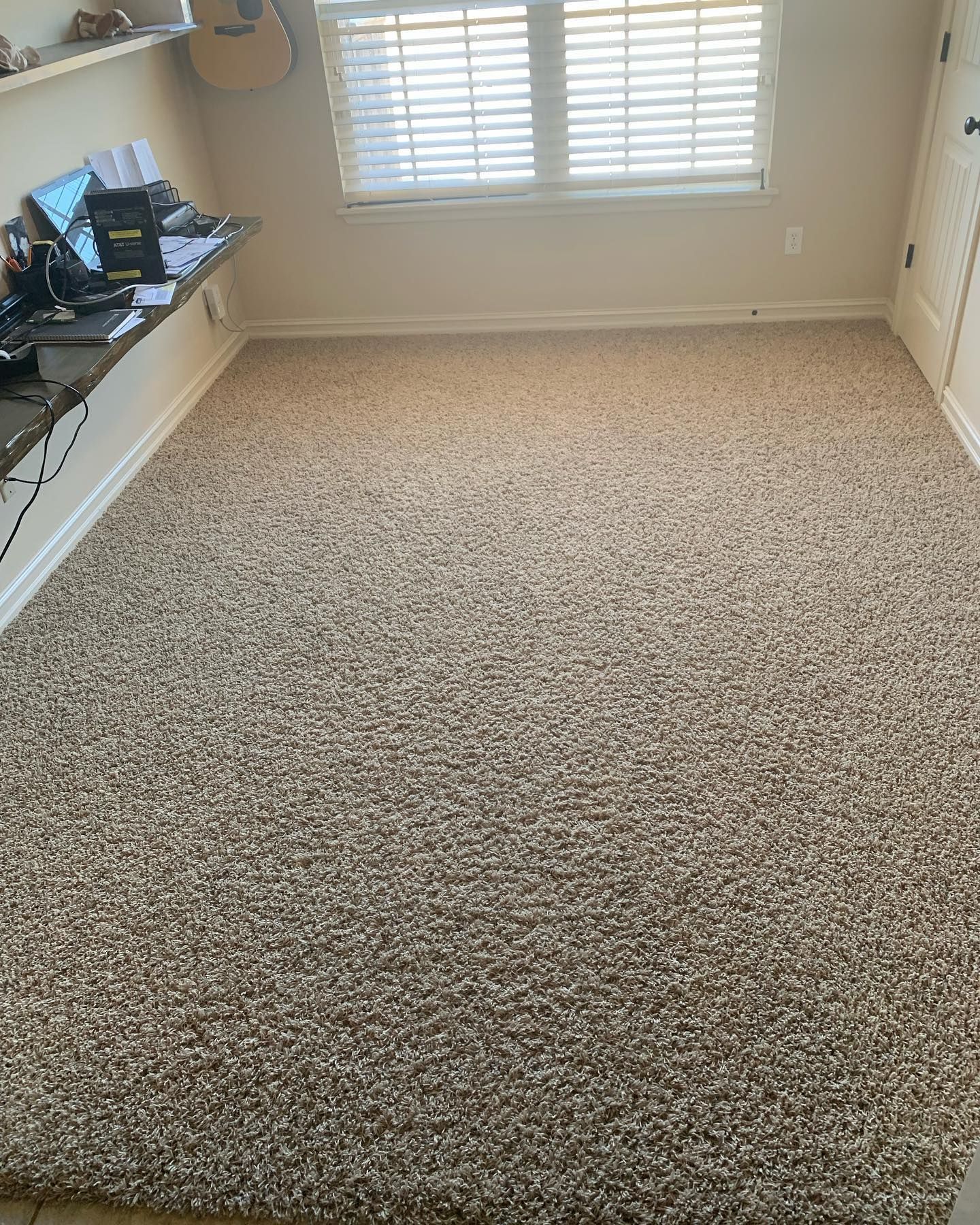 A large carpeted floor in a room with a desk and a window.