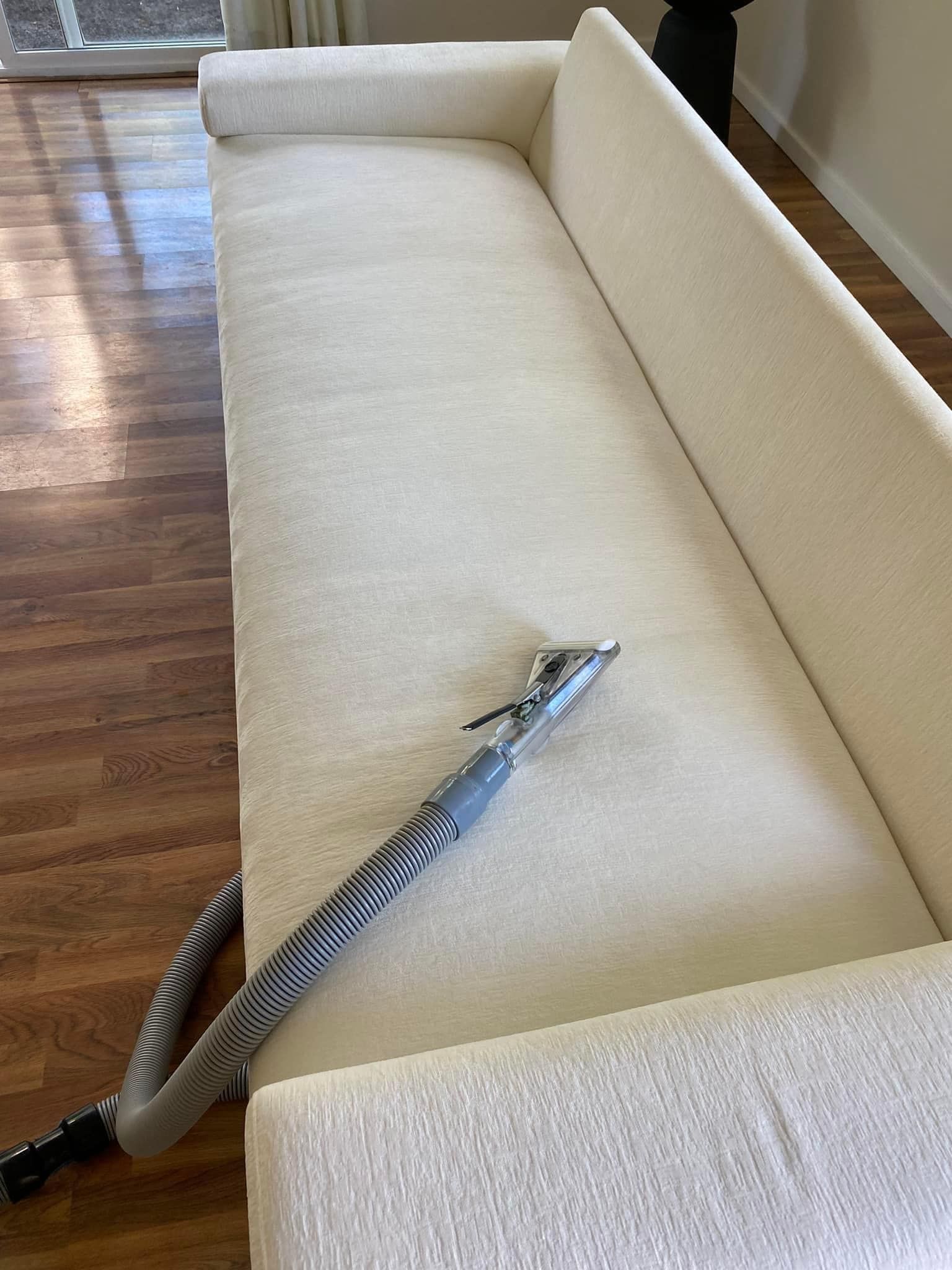 A white couch with a vacuum hose attached to it in a living room.