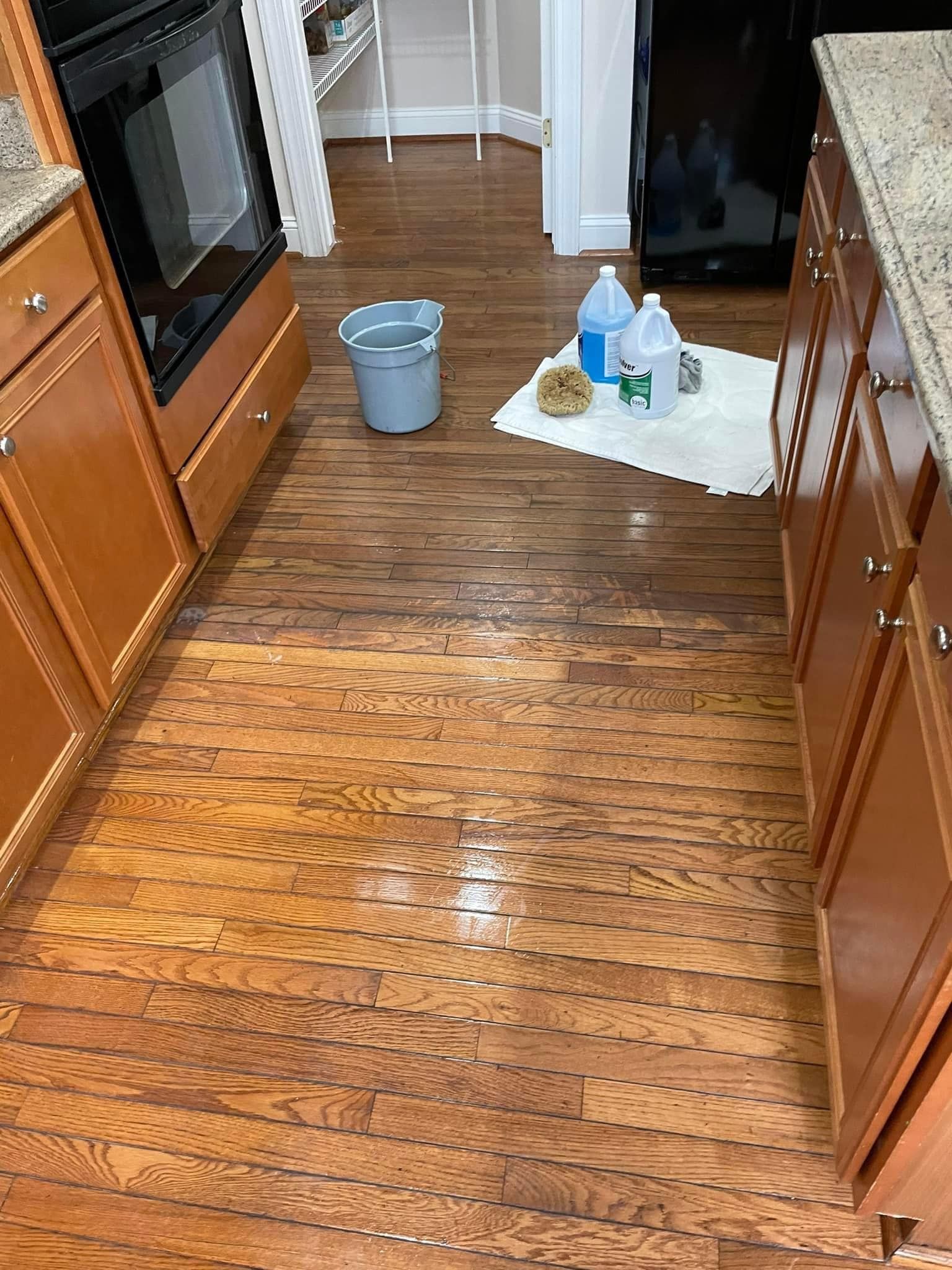 A kitchen with wooden floors , cabinets , a bucket and a bottle of water on the floor.