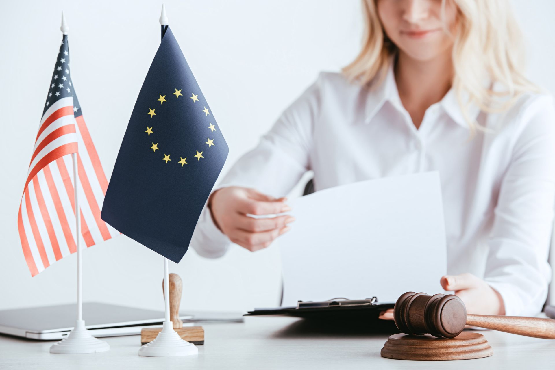 Person holding a document beside EU and U.S. flags with a judge’s gavel on a desk