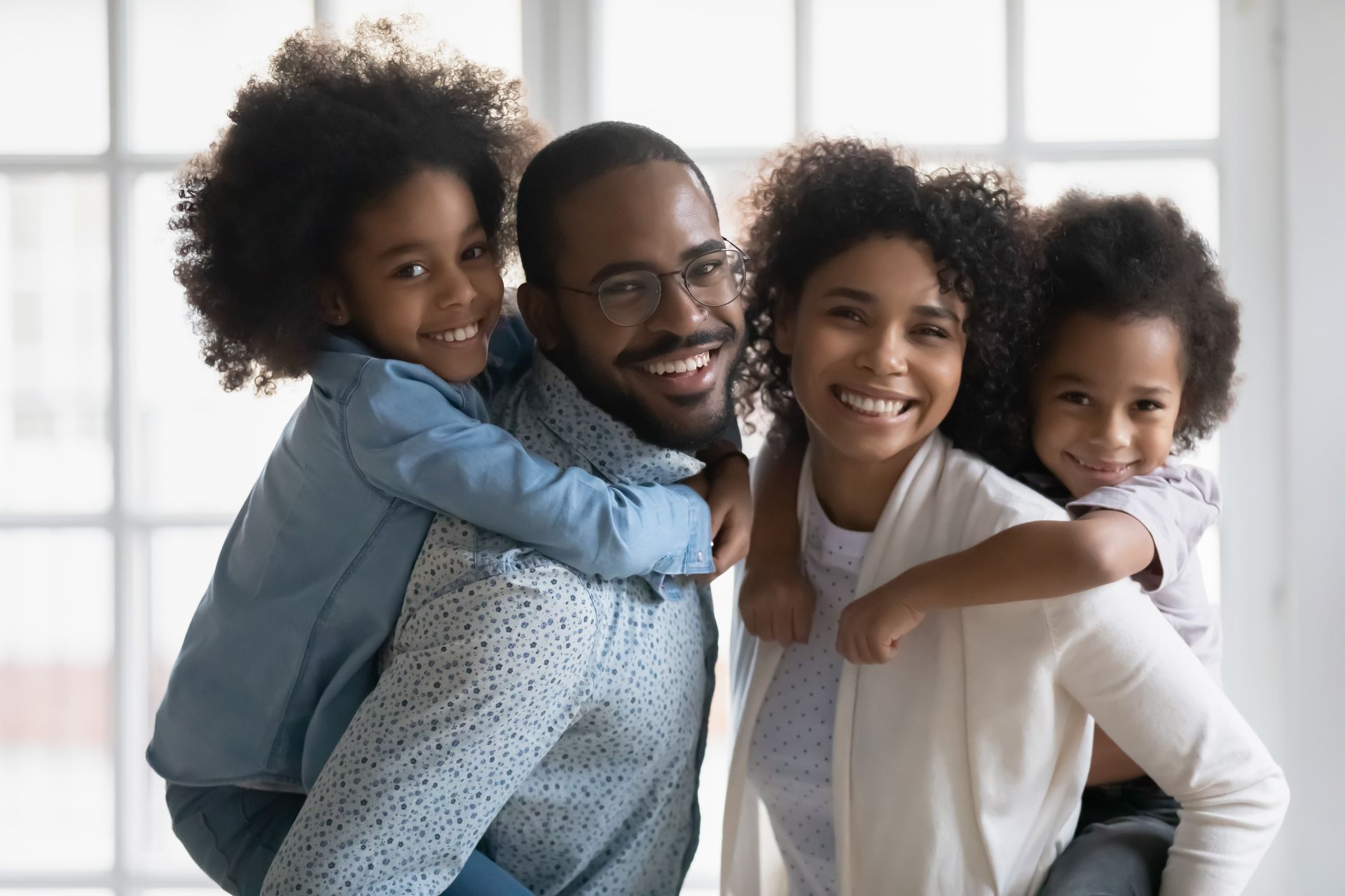Smiling family of four hugging on a bright couch near a window