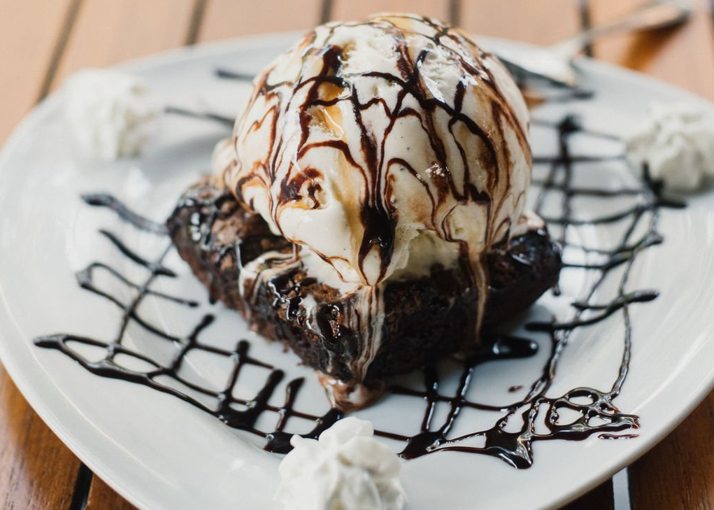 A brownie with ice cream and chocolate sauce on a white plate.