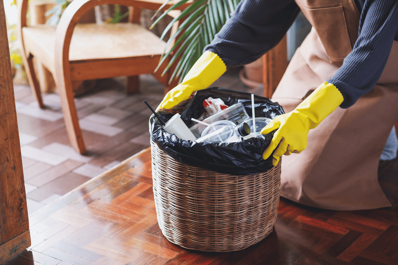 A person wearing yellow gloves is putting trash in a basket.