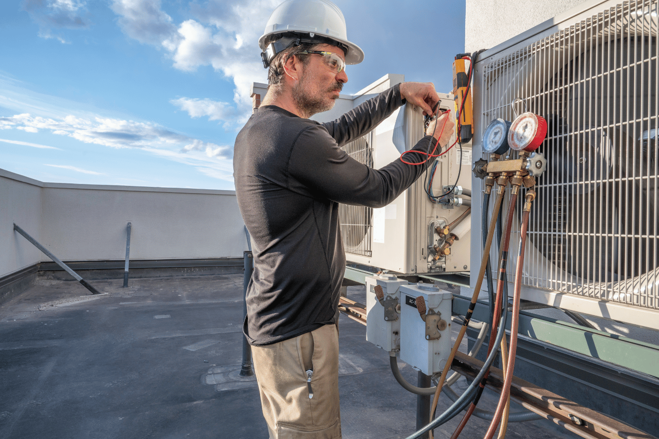 A man is working on an air conditioner on the roof of a building.