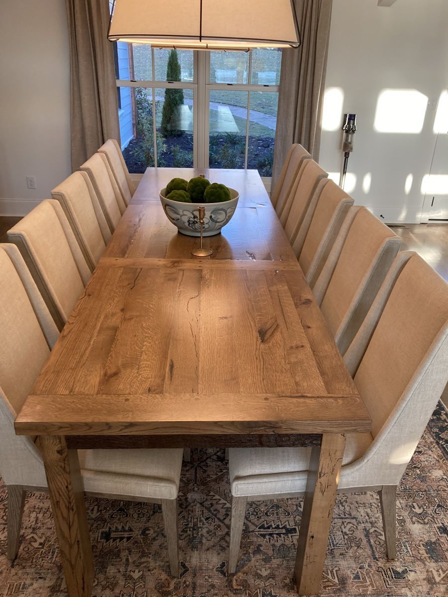 Wooden dining table with beige chairs in a bright room, with a centerpiece and window view.