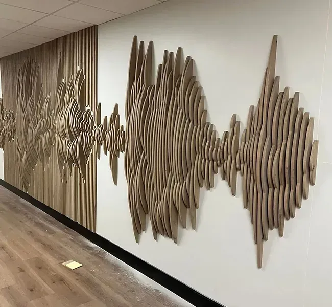 Wooden abstract wall sculpture on a white hallway wall above a wood floor