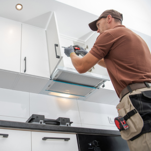 Technician installing a stainless steel range hood in a white kitchen