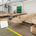 Woodworking shop with large timber beams, a saw table, and stacked lumber on pallets