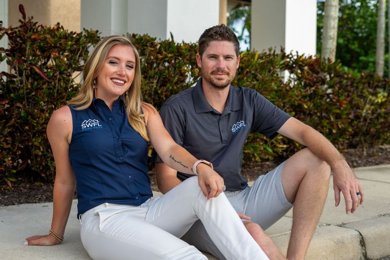 Woman and man sitting outside, smiling. Woman in navy shirt and white pants, man in gray shirt and shorts.