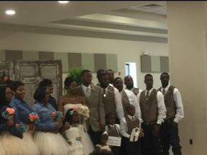 Group of people posing indoors at a wedding, with bridesmaids holding colorful bouquets and men in suits.