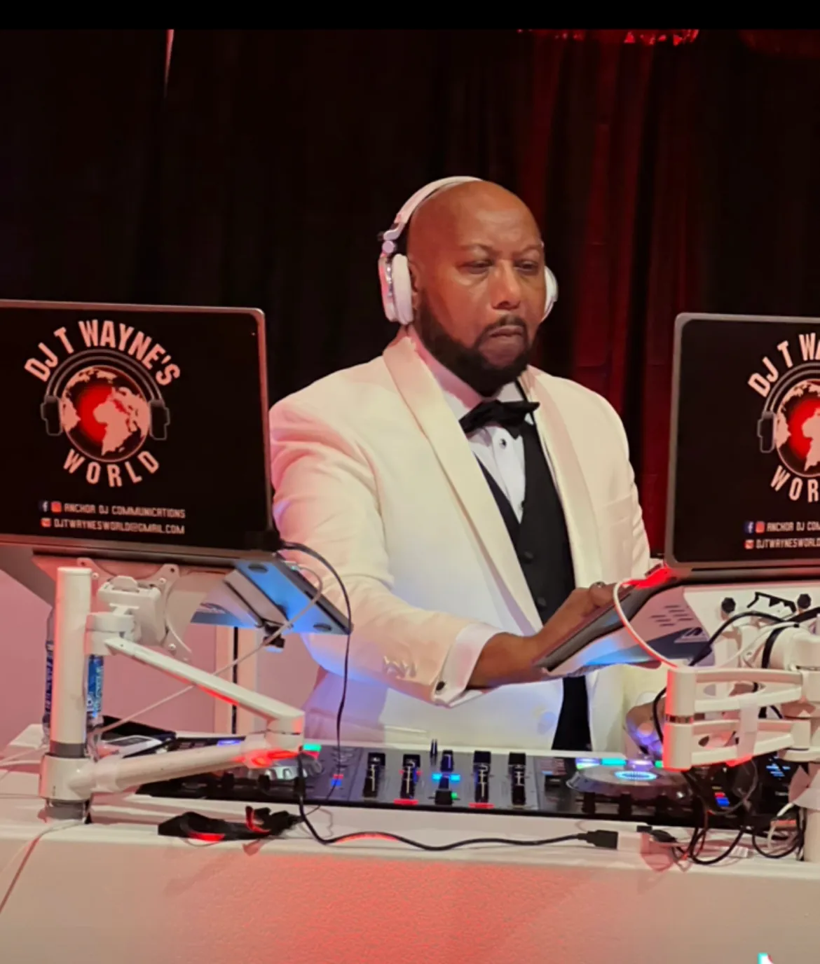 DJ in a white tuxedo and headphones, mixing at a DJ booth with glowing equipment and laptop screens
