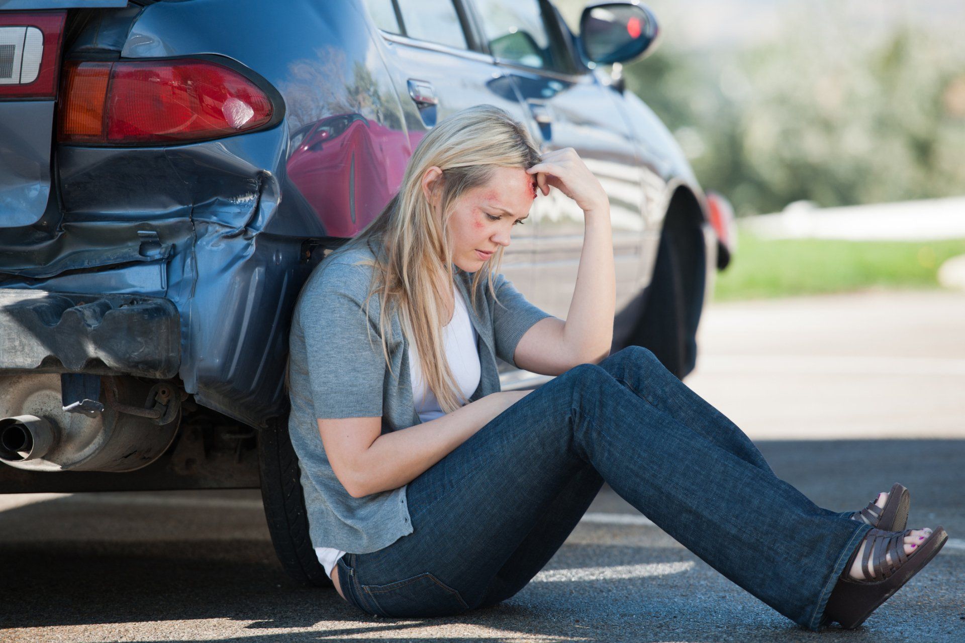 Woman sitting on the ground, injured after a car crash