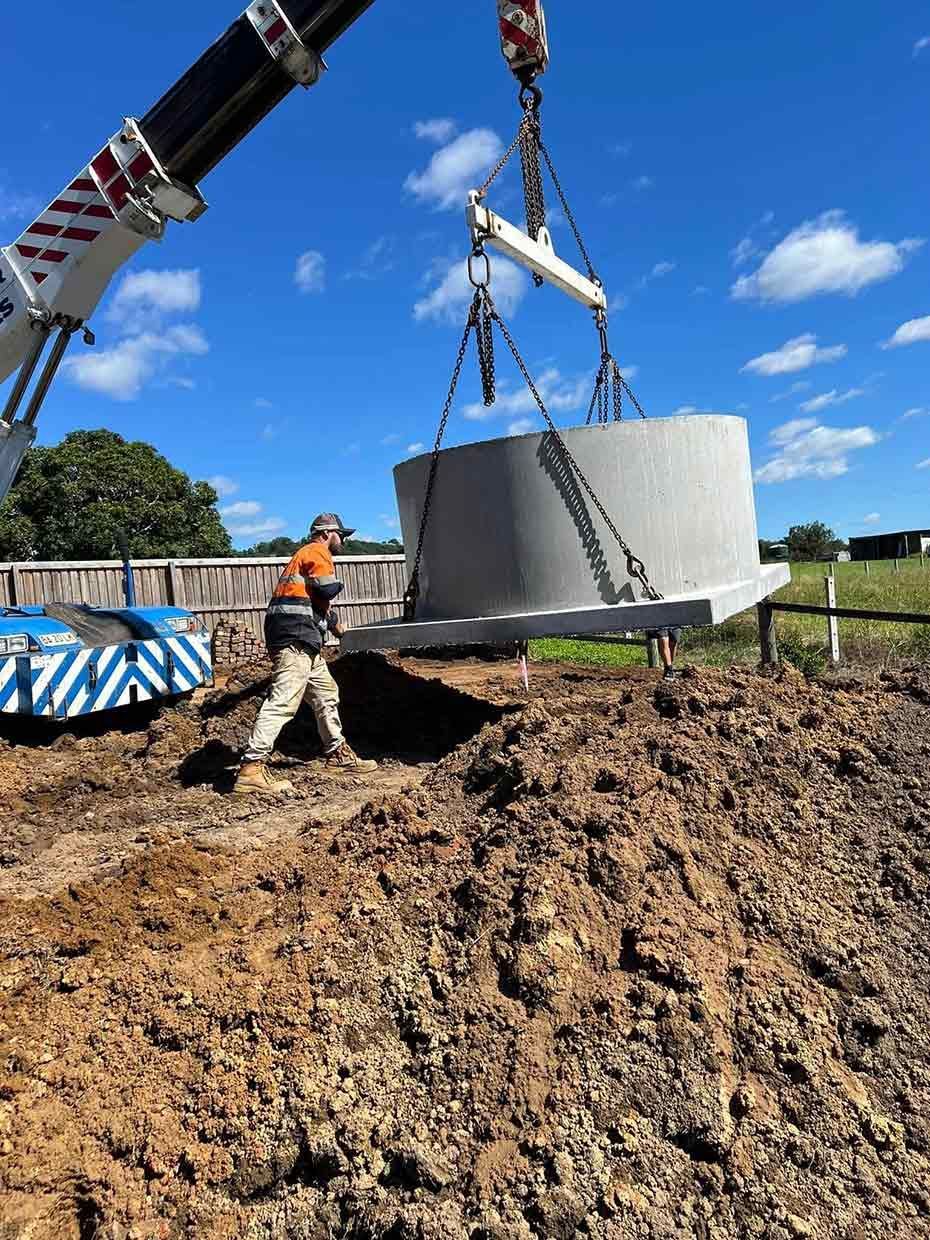 A Man is Standing in the Dirt Next to a Crane Lifting a Large Concrete Object — Etosha Plumbing & Gasfitting In Alstonville, NSW