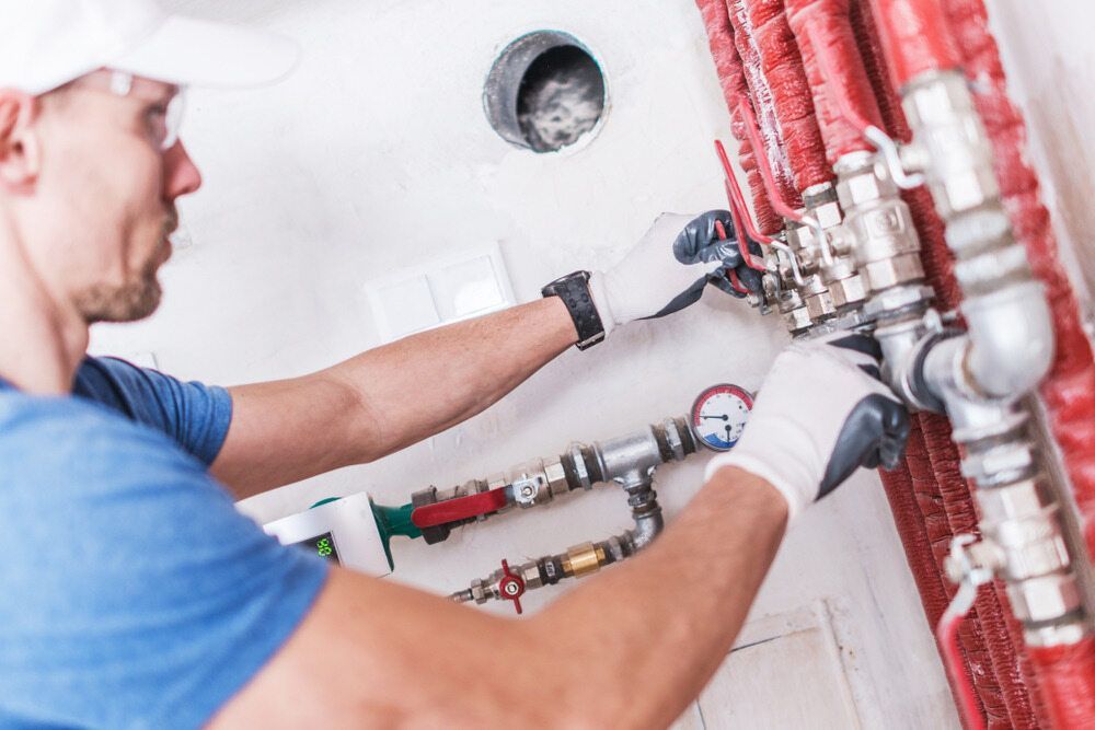 A Person Is Holding A Pipe Under A Sink In A Bathroom — Etosha Plumbing & Gasfitting In Alstonville, NSW