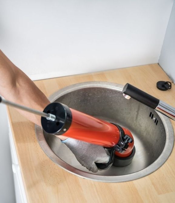A Person Is Holding A Pipe Under A Sink In A Bathroom — Etosha Plumbing & Gasfitting In Casino, NSW