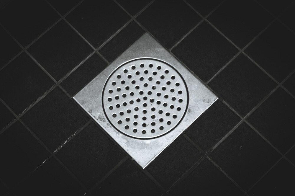 A Square Drain With Holes In It Is On A Black Tiled Floor — Etosha Plumbing & Gasfitting In Alstonville, NSW