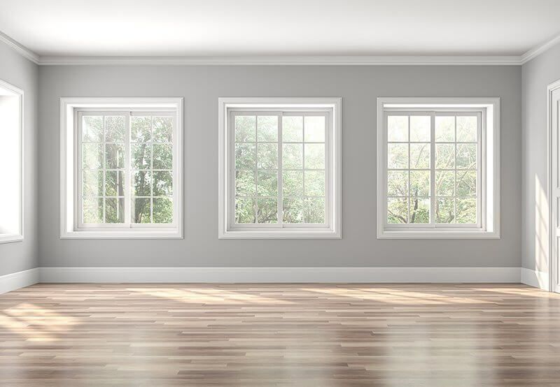 Bright empty room with three large windows and sunlight on wood floors