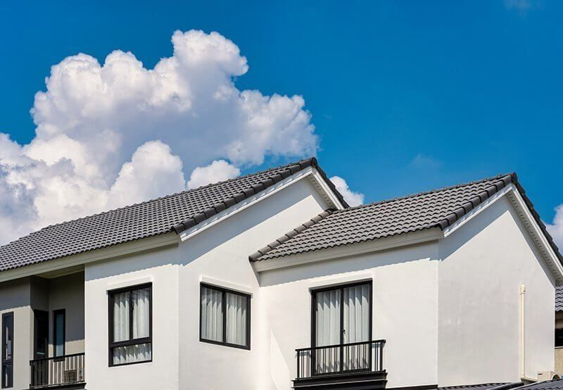 Modern white houses with gray roofs under a bright blue sky and clouds