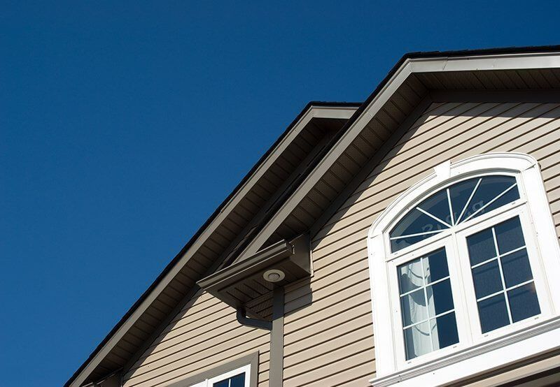 White-trimmed house roof and arched window against a clear blue sky