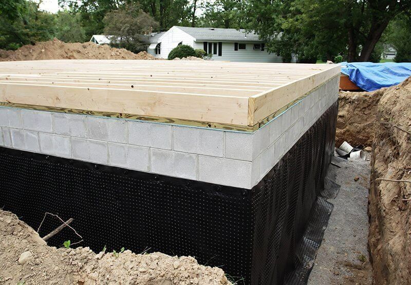 Concrete block foundation under construction with wooden framing and black waterproofing membrane outdoors