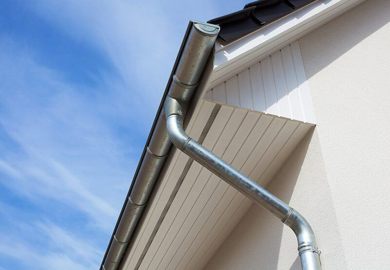 Metal rain gutter and downspout on a white house against a blue sky