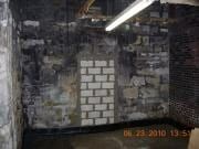 Damp, dark basement wall with a small patch of white bricks and a fluorescent light overhead