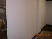 White wall and corner of a room with a dark doorway on the left, dimly lit.