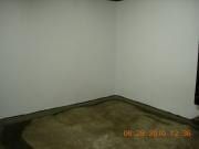 Empty room corner with white walls, dark baseboards, and a gray carpet floor.