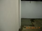 Dim hallway with white walls and a doorway opening to a darker room with green floor.