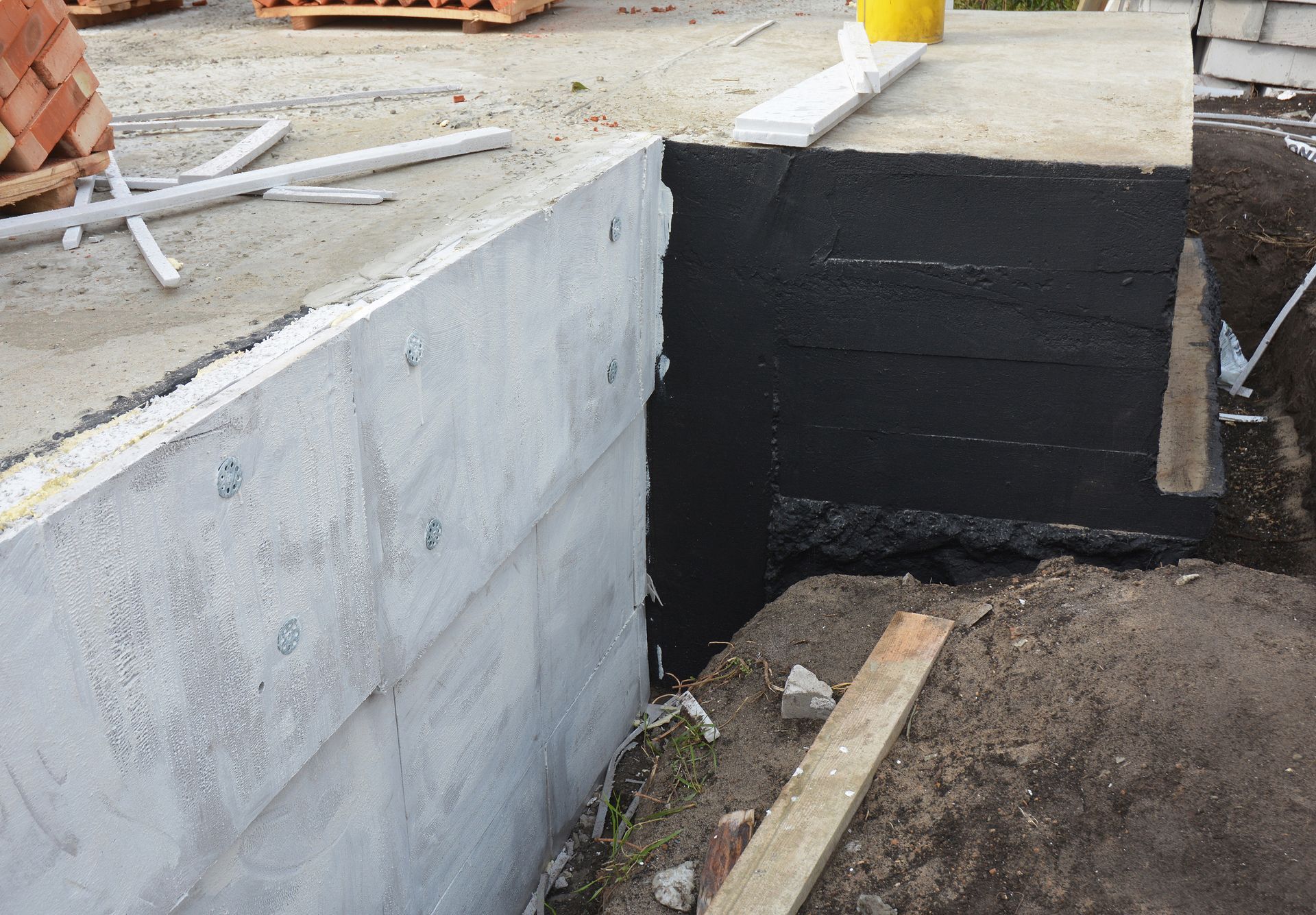 Partially built concrete foundation wall with black waterproofing and dirt trench beside it Partially built concrete foundation wall with black waterproofing and dirt trench beside it