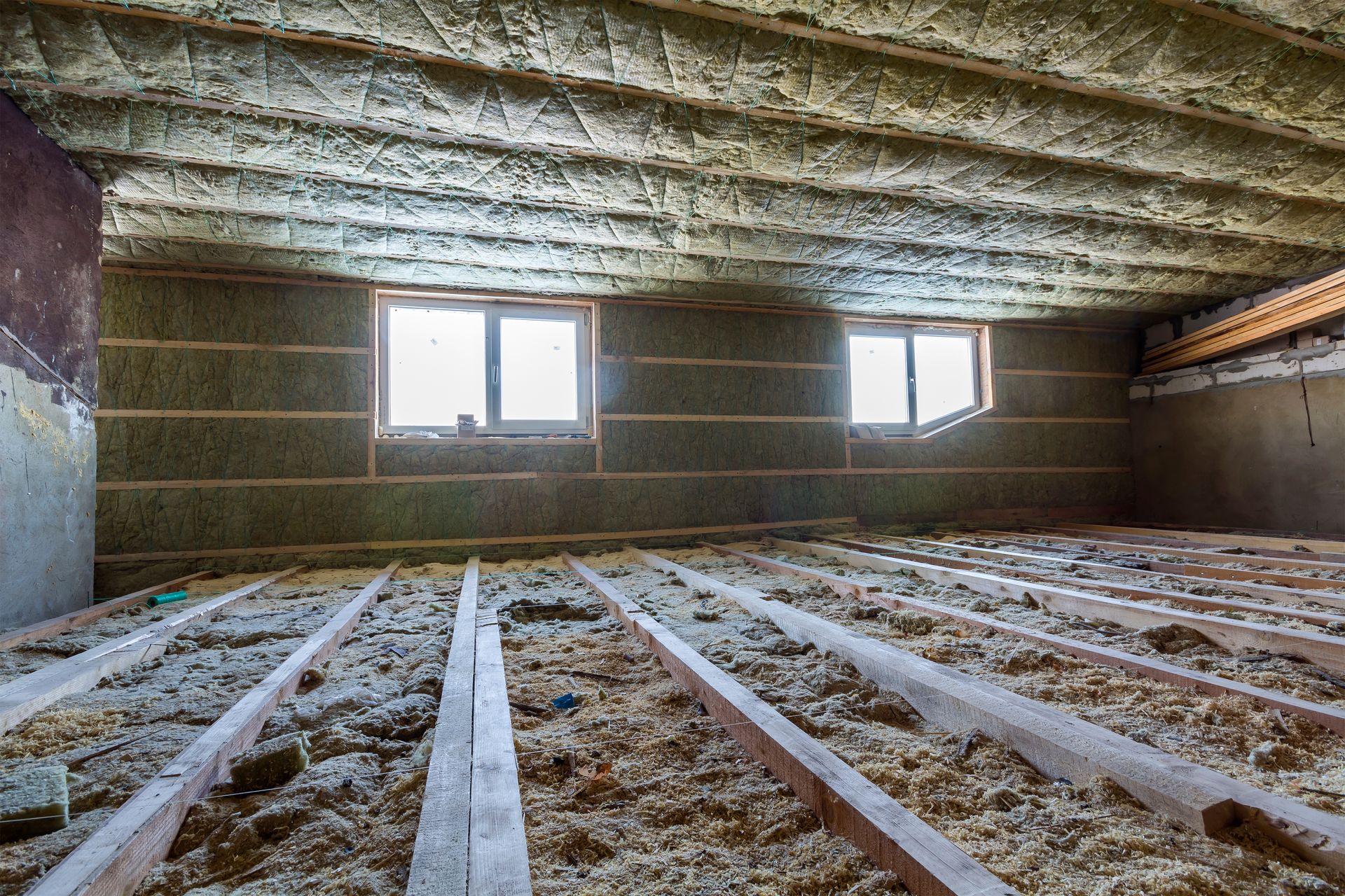 Insulated attic with exposed floor joists and two small windows letting in daylight Insulated attic with exposed floor joists and two small windows letting in daylight
