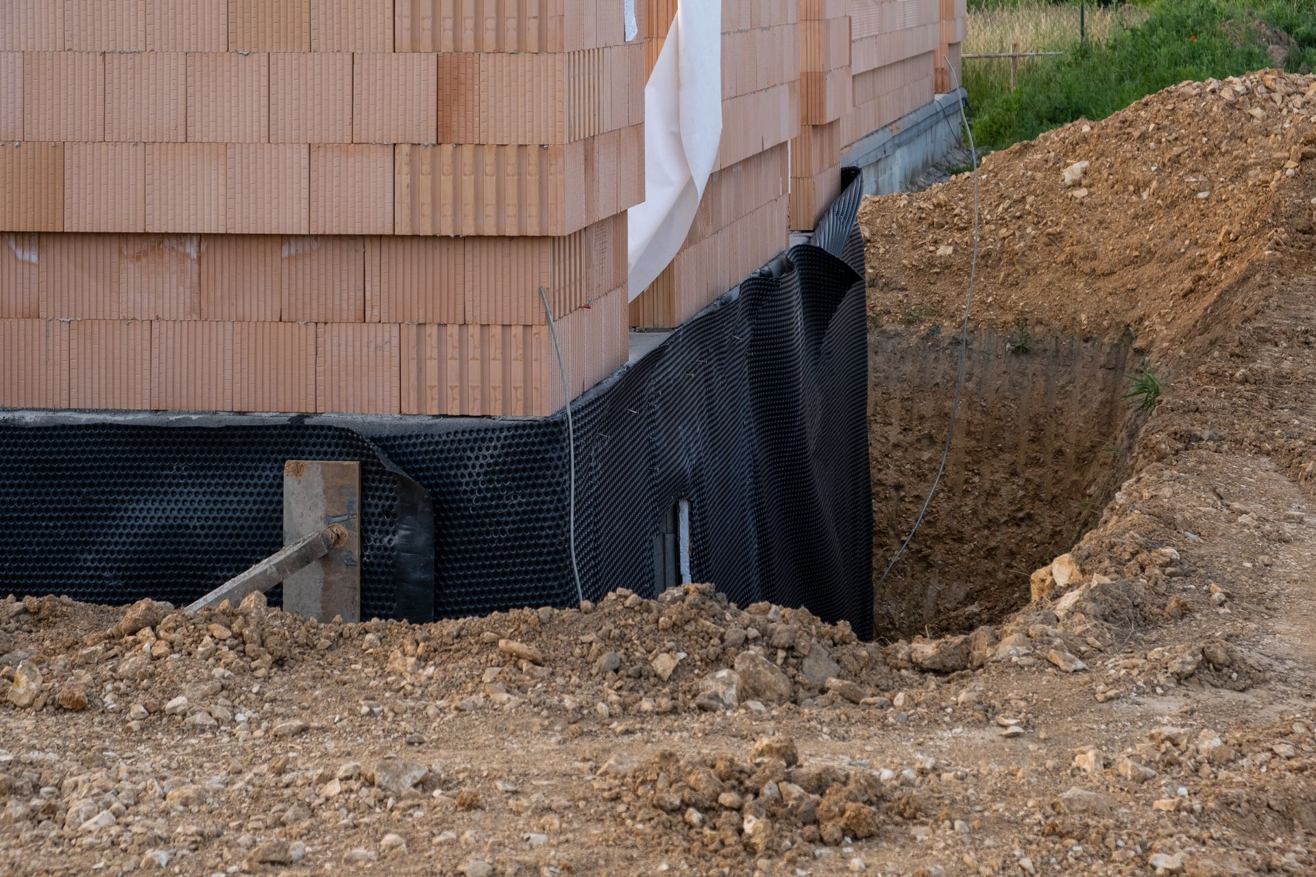 Construction site with brick wall foundation, black drainage membrane, and exposed dirt trench
