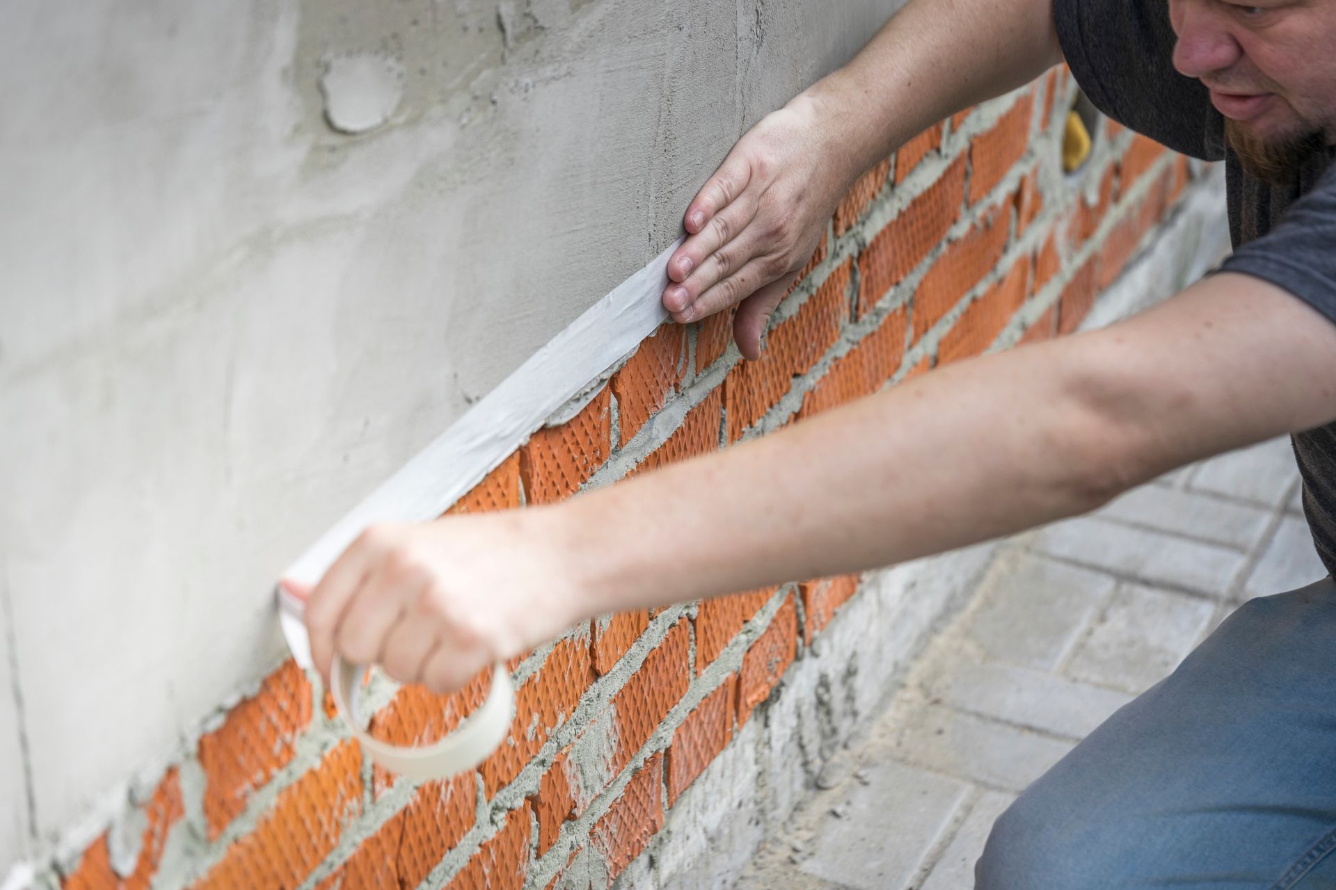 Person applying white trim to an orange brick wall during home construction