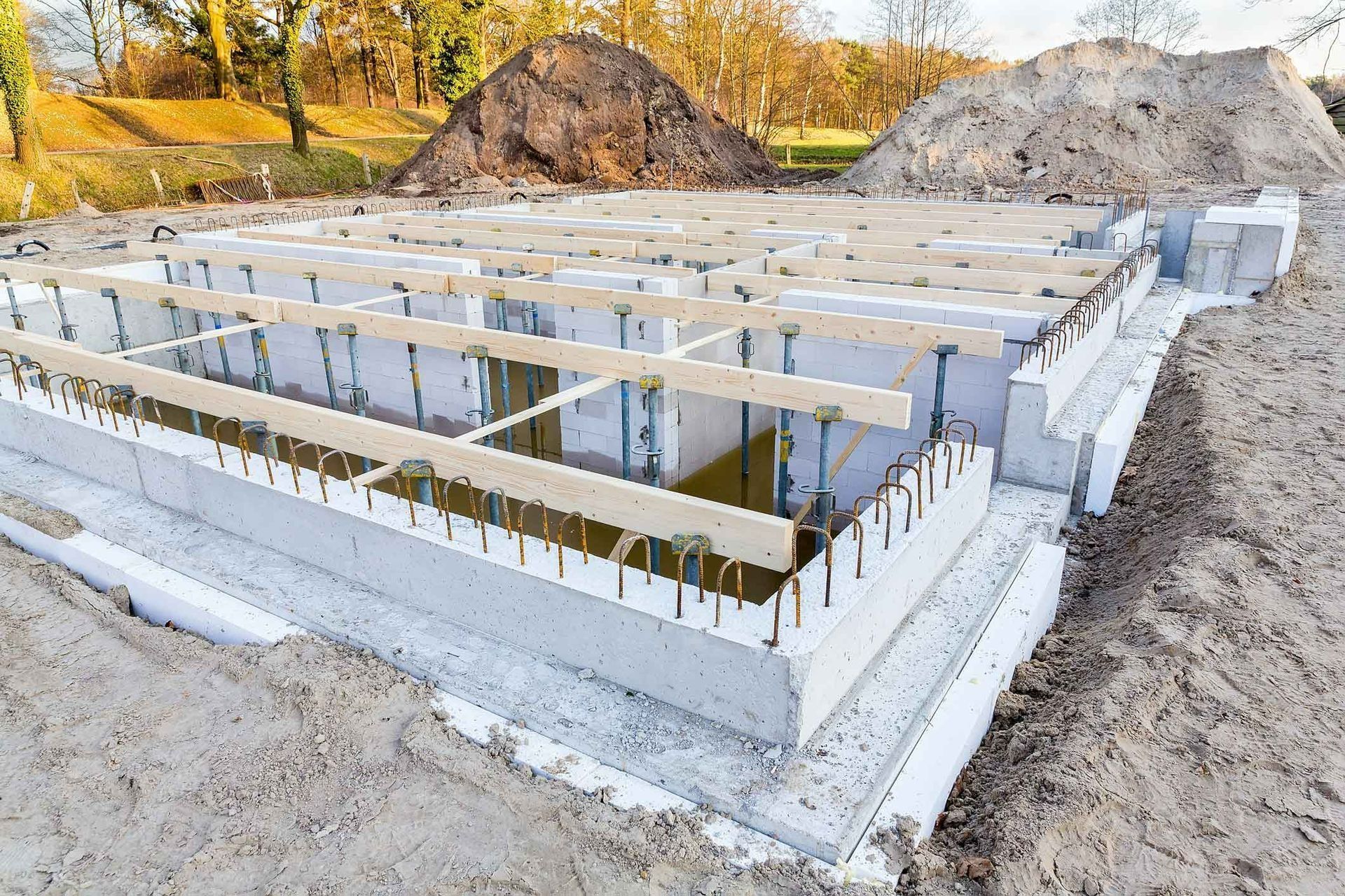 Concrete foundation under construction at a rural site, with wooden framing and autumn trees in the background