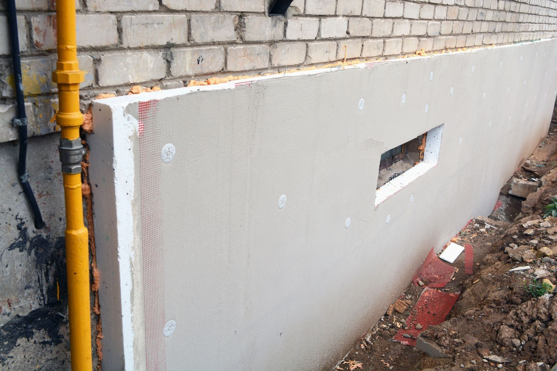 Gray panel leaning against a brick wall beside a yellow pipe in an outdoor construction area