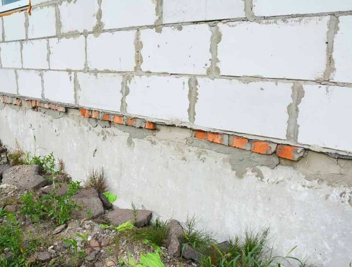 Partially built cinder block wall with exposed orange bricks and weeds at the base Partially built cinder block wall with exposed orange bricks and weeds at the base