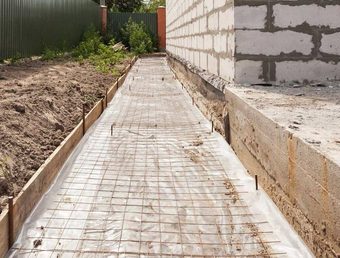 Concrete walkway under construction beside a cinder block wall and dirt trench outdoors