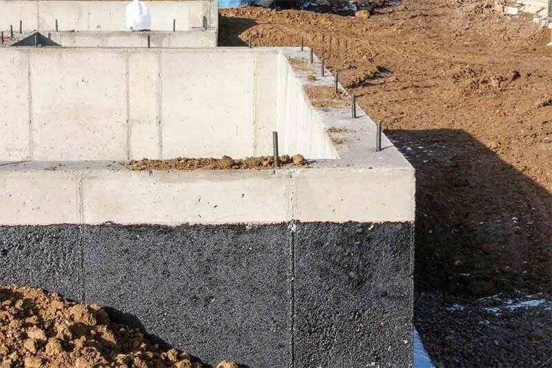 Concrete foundation wall with black waterproofing coating on a dirt construction site